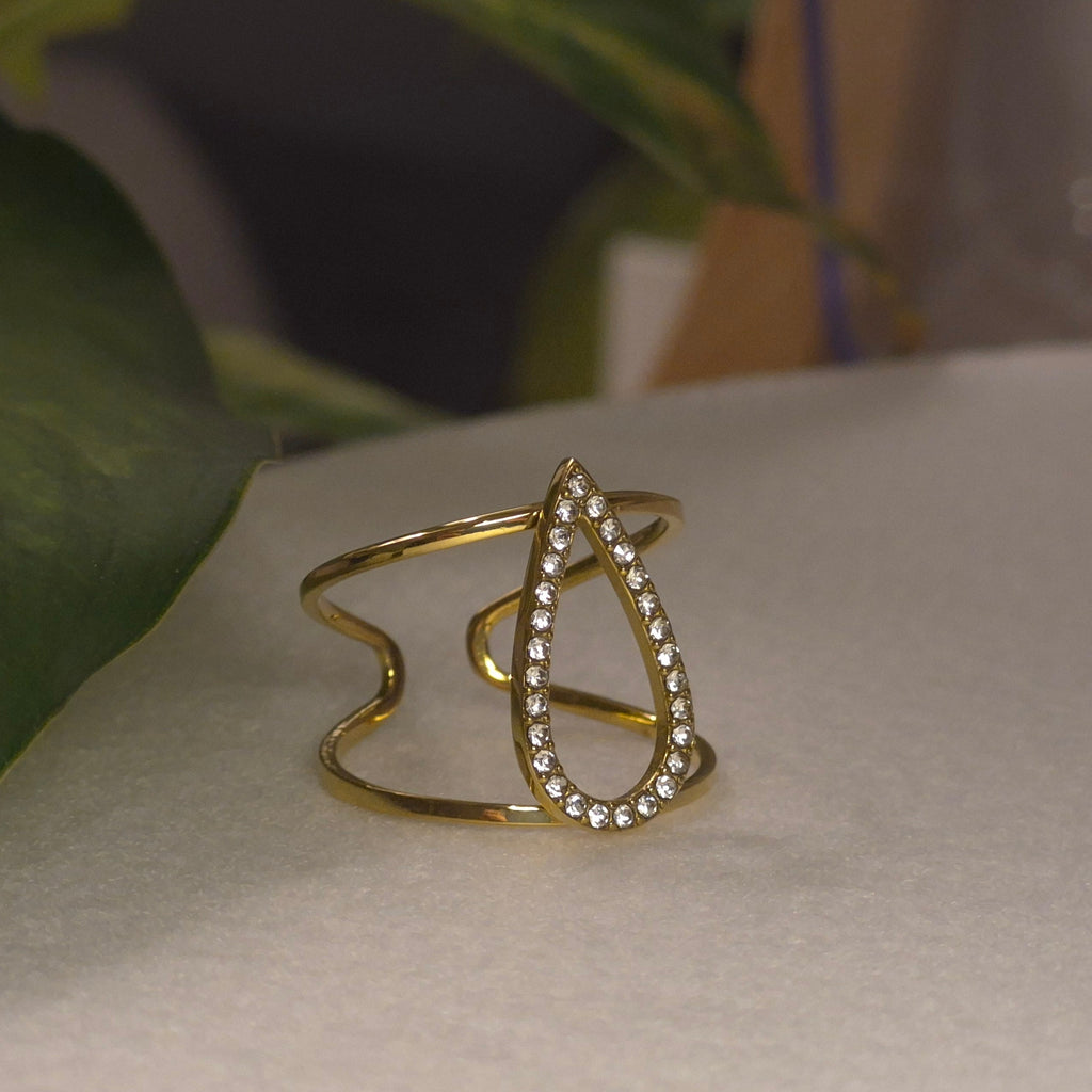 Bague large dorée ajustable et ajourée avec un motif central en forme de goutte évidée pavée de strass brillants.