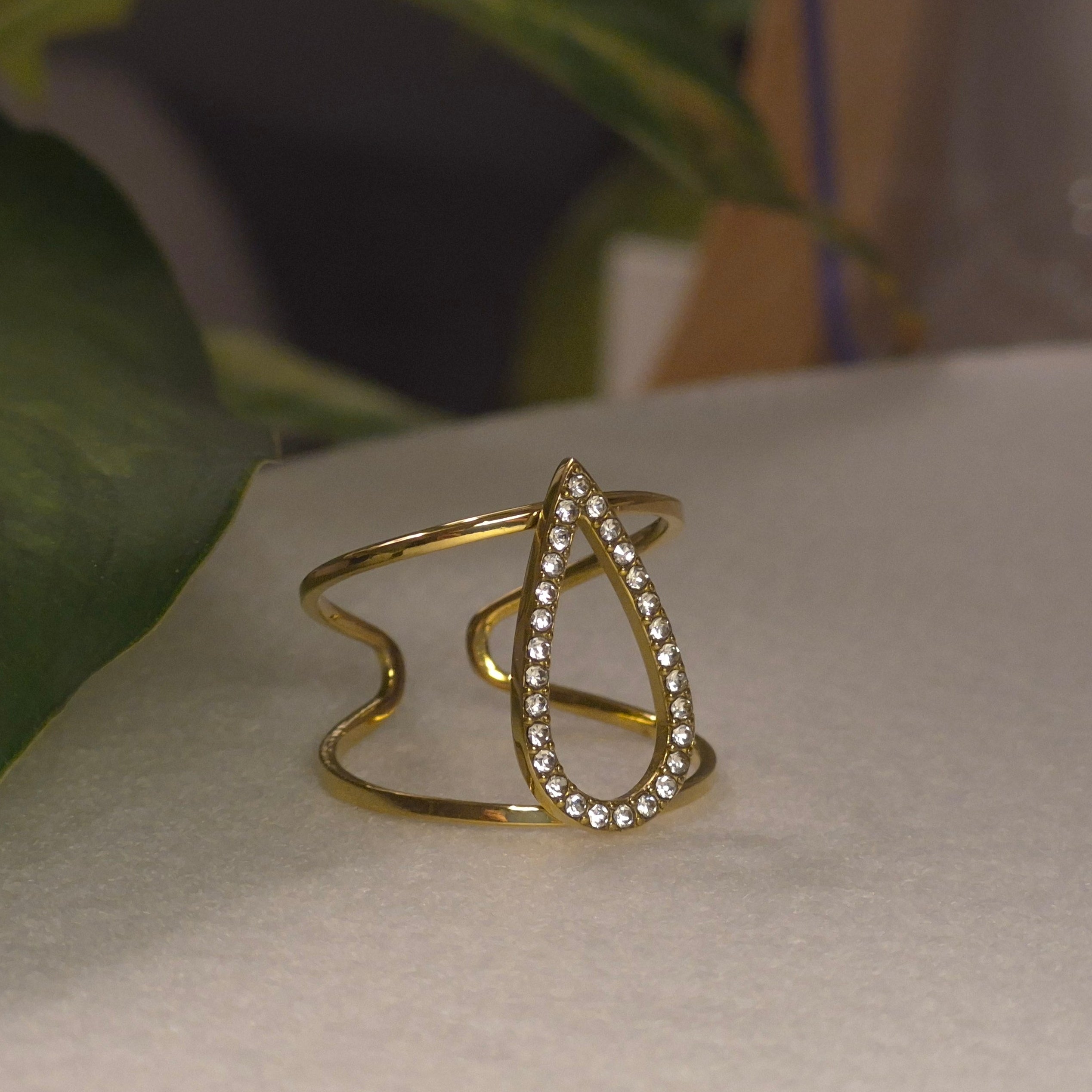 Bague large dorée ajustable et ajourée avec un motif central en forme de goutte évidée pavée de strass brillants.