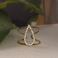 Bague large dorée ajustable et ajourée avec un motif central en forme de goutte évidée pavée de strass brillants.