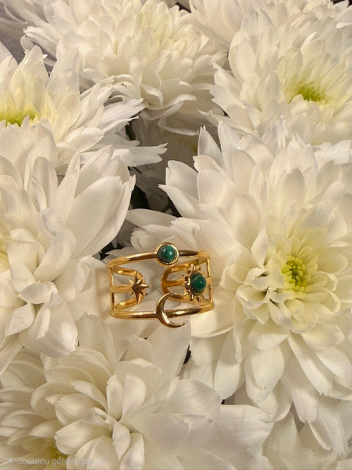 Bague large dorée ajustable et ajourée avec motifs lune, soleil et étoile, sertie de deux pierres rondes vert foncé.