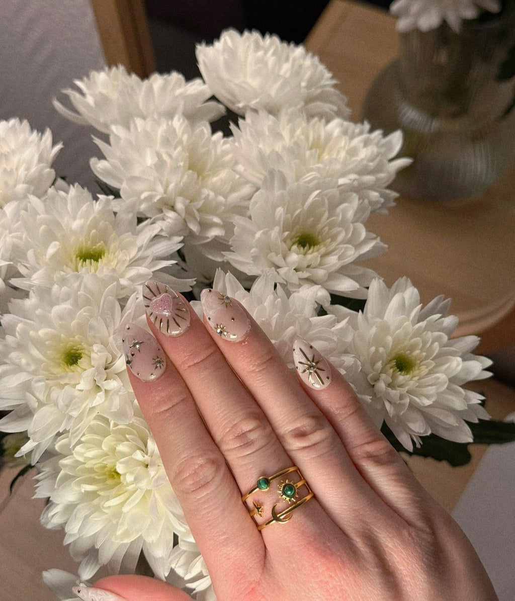 Bague large dorée ajustable et ajourée avec motifs lune, soleil et étoile, sertie de deux pierres rondes vert foncé.