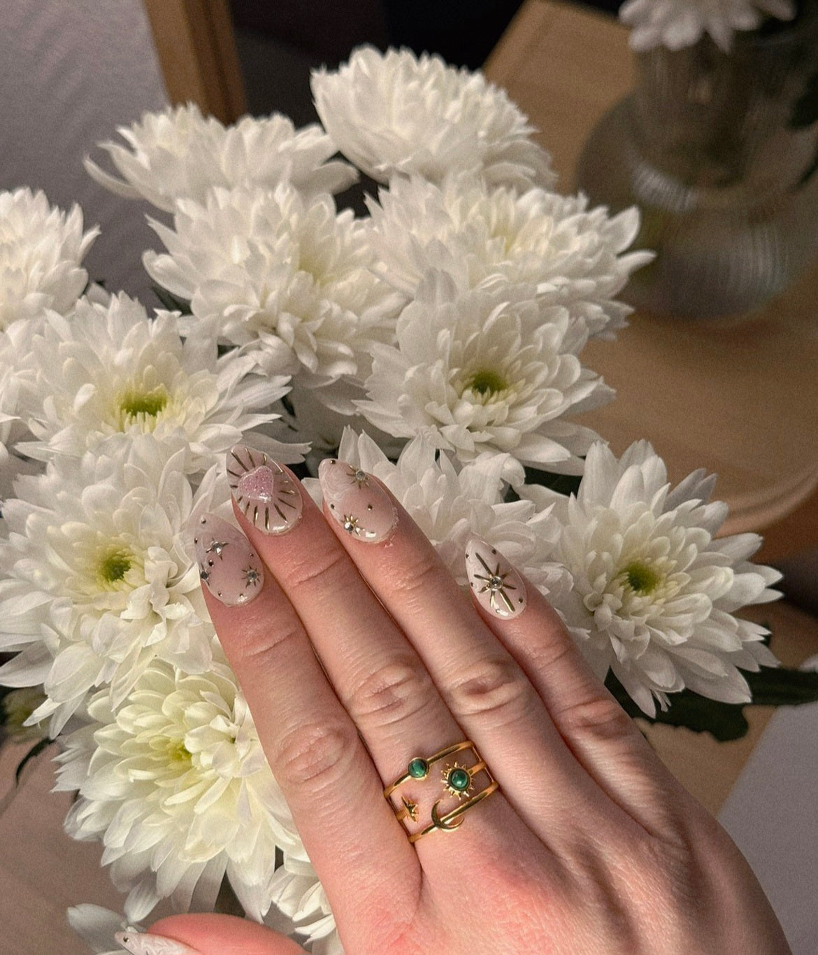 Bague large dorée ajustable et ajourée avec motifs lune, soleil et étoile, sertie de deux pierres rondes vert foncé.