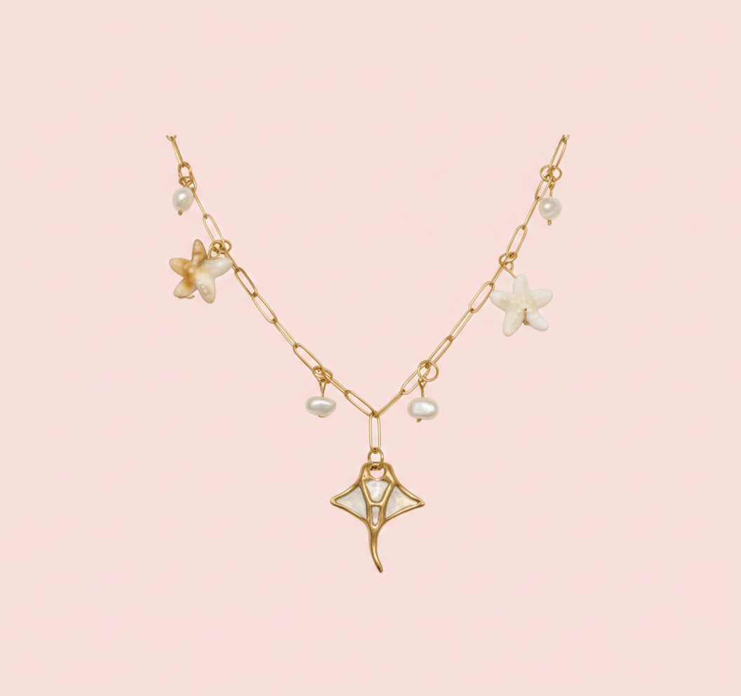 Collier doré à maillons rectangulaires avec un grand pendentif raie manta, orné d'étoiles de mer nacrées et de perles d'eau douce, sur fond rose clair.