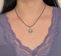 Collier en fines perles de couleur acrylique violette avec un pendentif en étoile d'argent stylisée, porté sur un décolleté avec un haut en dentelle.