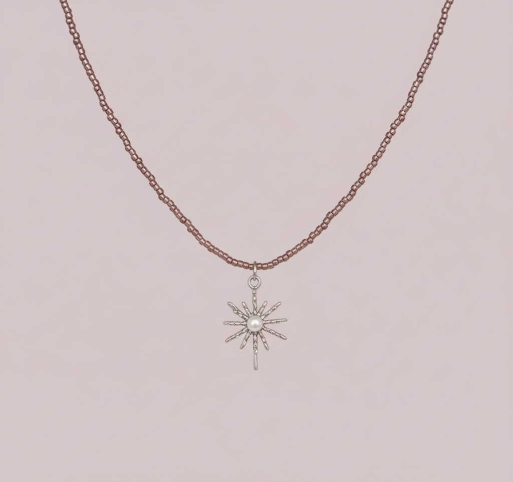 Collier en fines perles de couleur acrylique violette avec un pendentif étoile en métal argenté orné d'une perle blanche au centre, sur fond rose clair.