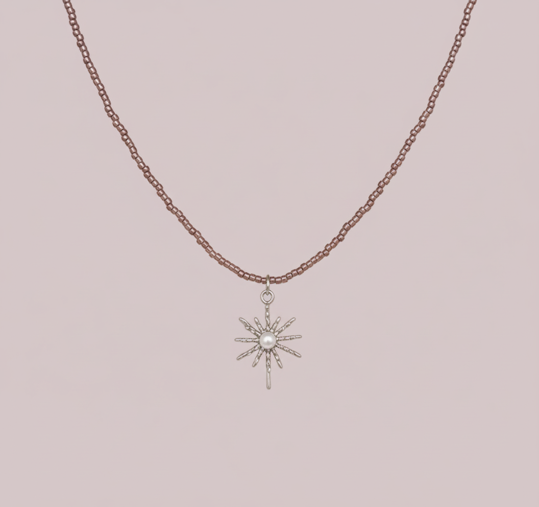 Collier en fines perles de couleur acrylique violette avec un pendentif étoile en métal argenté orné d'une perle blanche au centre, sur fond rose clair.
