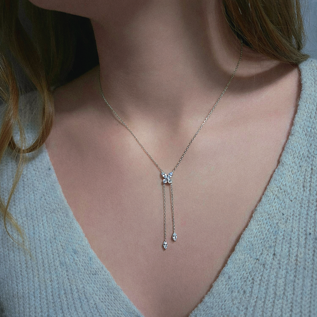 Collier cravate argenté avec pendentif papillon en strass et deux fines chaînettes pendantes terminées par des cristaux en forme de goutte.