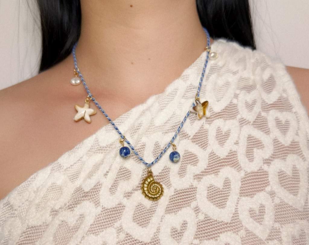 Collier en cordon tressé bleu et blanc avec pendentif coquillage doré, perles bleues et breloque étoile de mer.